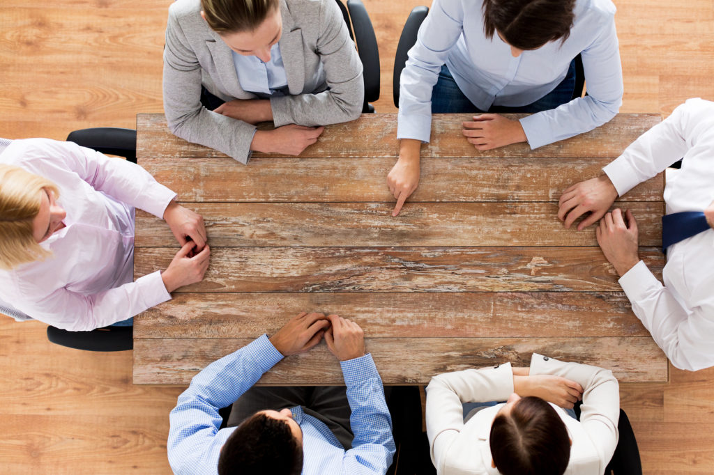 business, people and team work concept - close up of creative team sitting at table and pointing finger to something in office